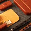 A styled flat-lay of leather duduk reed case on a gray felt surface, including a brown leather reed case case and parts of a dark wooden duduk.