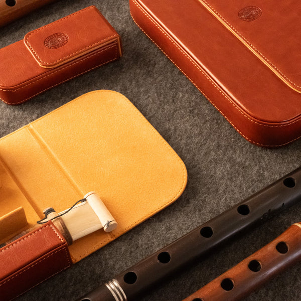 A styled flat-lay of leather duduk reed case on a gray felt surface, including a brown leather reed case case and parts of a dark wooden duduk.