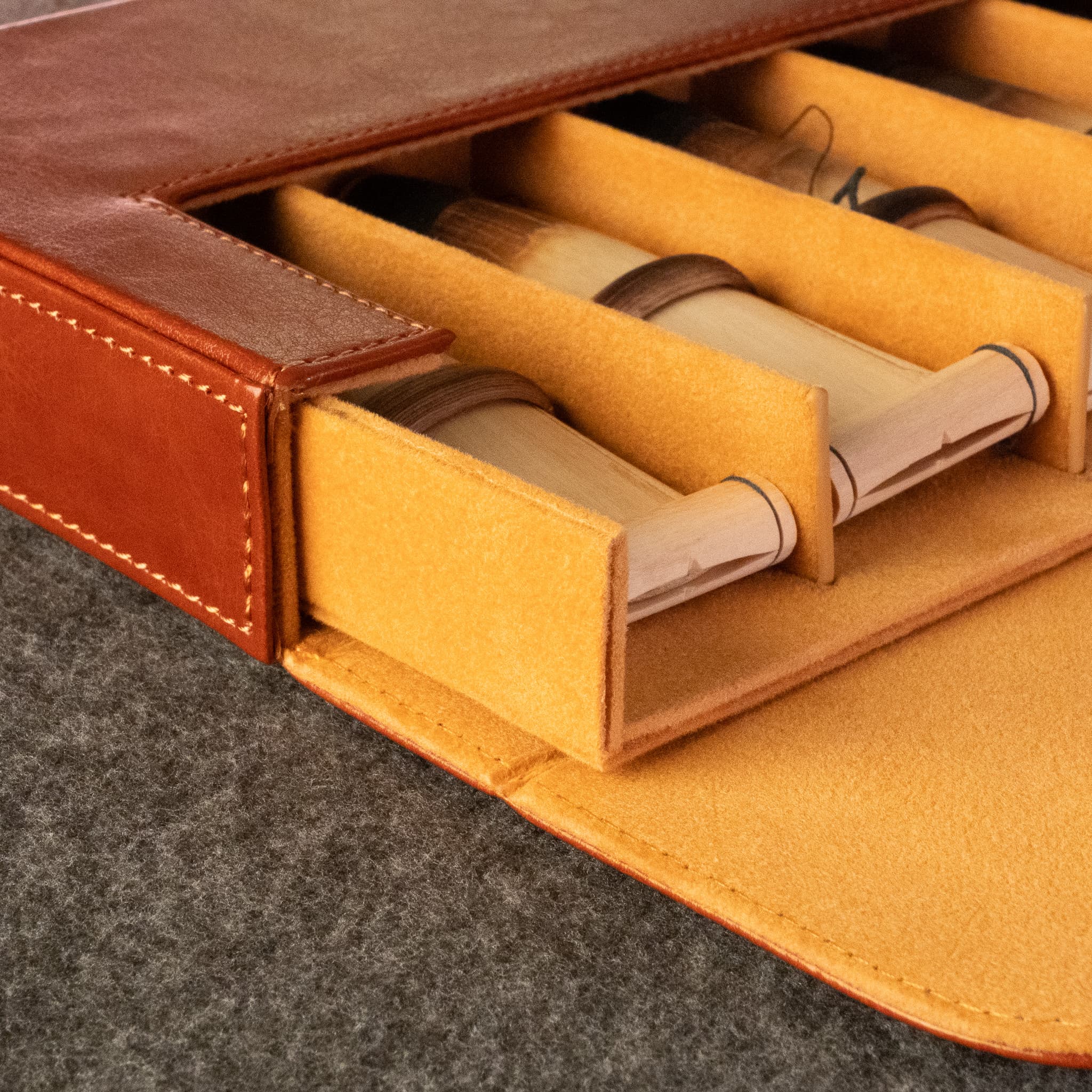Close-up of a brown leather duduk reed case by Dudukhouse with a mustard-yellow felt interior, showing several duduk reeds stored in compartments.
