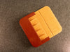 A square Dudukhouse leather duduk reed case with a warm orange-brown exterior and a yellow-orange interior, shown open on a textured gray surface.
